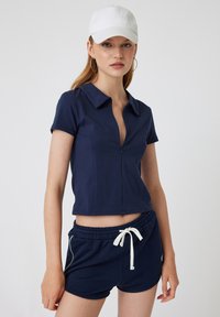 Marine blauwe polo-shirt met rits en korte mouwen, gecombineerd met bijpassende marine blauwe shorts met een elastische tailleband en witte koordaccenten.