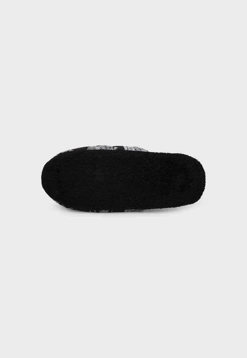 Black fuzzy slipper sole with a patterned upper edge visible on a plain light background.