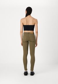 Jeans ajustados color verde oliva con una textura suave, diseño de cinco bolsillos y parche con logo en la parte trasera. Combinados con un top negro sin tirantes y zapatos negros.