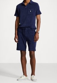 Mörkblå pikétröja och shorts-set i mjukt material, med bröstficka och elastisk midja. Matchas med vita sportiga sneakers.