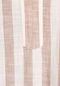 Béžová a biela látka s pruhmi a textúrovaným tkaním; v strede má špicatú kapsu. Pruhy majú rôznu šírku.