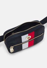 Borsa a tracolla in tessuto blu navy con zip dorate. Caratterizzata da un audace design a strisce rosse, bianche e blu e un emblema circolare in metallo con marchio.