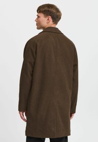 Brun ullfrakk med rett snitt, notched krage og lange ermer. Har en glatt tekstur og rene sømdetaljer på baksiden.