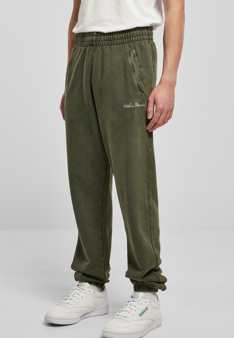 Olivno zeleni flis jogger hlače z elastičnim pasom, stransko žepom in rebrastimi manšetami. Na sprednji strani je vezen napis "Urban Classics".
