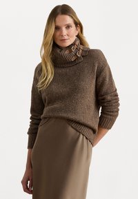 Hnedý pletený sveter s vysokým rebrovaným golierom, s koženými akcentmi a voľným strihom, doplnený o elegantnú béžovú sukňu.