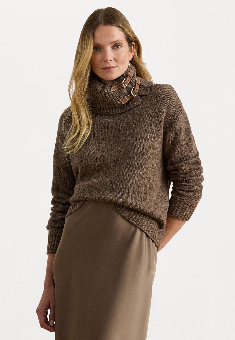 Hnedý pletený sveter s vysokým rebrovaným golierom, s koženými akcentmi a voľným strihom, doplnený o elegantnú béžovú sukňu.