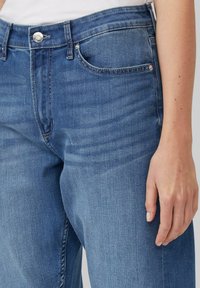 Modré riflové džínsy so strihom rovnej nohy, majúce zips a gombík na zapínanie, päť vreciek a jemné žehlenie na látke. Textúrovaný, stredne ťažký materiál.