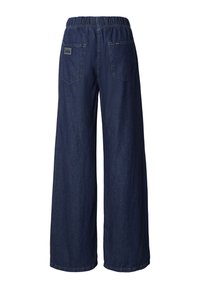 Tamsiai mėlynos spalvos plėšiotos džinsinės plačios kelnės su elastinga liemene ir dviem galinėmis kišenėmis su etikete. Lygus audinys, laisvas siluetas.