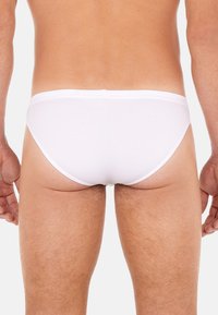 Weiße Baumwollslips mit einem niedrigen Schnitt, glatter Textur und elastischem Bund, die eine minimalistische und nahtlose Rückansicht zeigen.