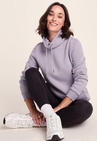 Light purple hoodie with a high collar and drawstrings, paired with black leggings and white sneakers. Smooth fabric, relaxed fit.