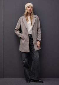 Abrigo de lana gris claro con solapas con muesca, botones de un solo botón y bolsillos laterales, combinado con jeans de pierna ancha negros y una diadema de punto beige.