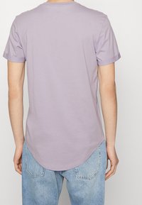 Fialové tričko s krátkým rukávem a kulatým lemem, vyrobené z měkké bavlny, s ohrnutými rukávy, kombinované se světle modrými džíny.