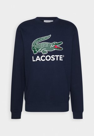 Sweatshirt bleu marine en mélange de coton, arborant un logo de crocodile vert bien en vue et le texte "LACOSTE" en blanc sur le devant. Encolure ras du cou et manches longues.