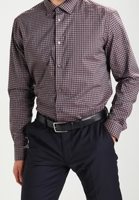 Camicia a maniche lunghe a quadri in borgogna e bianco, realizzata in tessuto intrecciato. Presenta un colletto button-down e bottoni frontali, abbinata a pantaloni neri.
