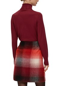 Burgunderfarbener Rollkragenpullover kombiniert mit einem karierten Minirock in roten, schwarzen und weißen Farbtönen aus einem strukturierten Stoff.