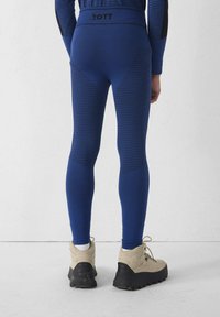 Blauwe sportlegging met horizontale strepen, hoge tailleband en vochtafvoerende stof. Gecombineerd met beige wandelschoenen.