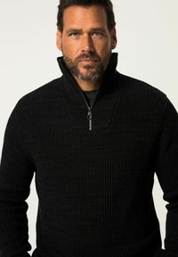 Maglione nero in maglia a treccia con zip a un quarto, dotato di texture a righe verticali. Presenta un colletto alto e un dettaglio con zip sullo scollo.