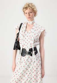 White dress with red cherry print, short flutter sleeves, tied neckline, and a black leather belt with silver accents. Black handbag.