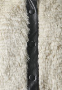 Gilet in pelliccia sintetica con una texture crema, dotato di un davanti in pelle nera e grandi bottoni rotondi lungo il centro.