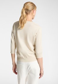 Maglione di maglia beige chiaro con maniche a tre quarti, tessuto texturizzato, orlo e polsini a costine, abbinato a pantaloni bianchi a vita alta.