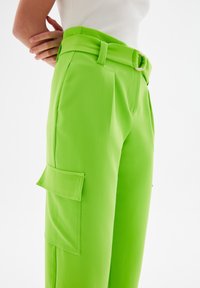 Heldergroene wijde broek van een zachte stof, met een hoge taille en riem, en een zijzak met gestikte details.