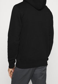 Zwarte hoodie met relaxte pasvorm, voorzien van een kangaroemand en geribbelde manchetten. Gemaakt van zacht, gestructureerd materiaal voor comfortabel dragen.