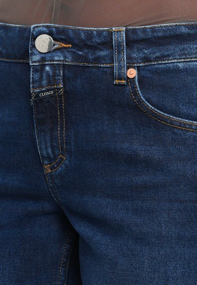 Denim jeans in dark indigo with a classic cut. Features copper buttons and contrasting orange stitching. Tag reads "CLOSED."