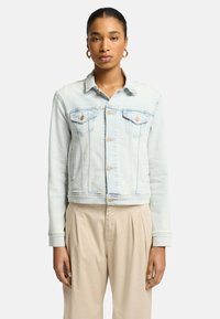 Lyseblå denimjakke med en kortet snit, brystlommer og guldknapper. Har en klassisk krave og lange ærmer med knapmanchetter.