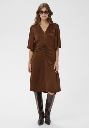 Braunes Kleid mit kurzen Ärmeln, V-Ausschnitt, gerafftem Detail an der Taille, kombiniert mit glänzenden, kniehohen Stiefeln aus dunkelbraunem Krokodil-Leder.