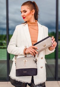 Beige quilted handbag with black leather base, gold accents, and detachable strap; matching flat wallet held in hand.