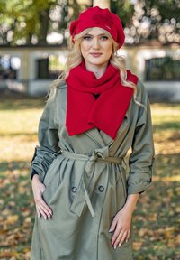 Olivi vihreä trench-coat, jossa on kaksiriviset napit, vyötärölle sidottu vyö, yhdistetty punaisen neulotun huivin ja kukilla koristellun matching-beretin kanssa.