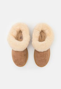 Brune semskede tøfler med en krämfärgad fårskinnskant och foder. Rund tådesign med en flat sula for komfort.
