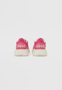 Pink athletic shoes with a textured upper and contrasting white sole. Features logo detail on heel and reinforced eyelets for laces.