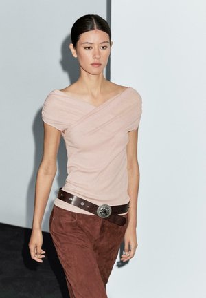 T-shirt fucsia aderente con maniche drappeggiate e design incrociato. Abbinata a pantaloni in suede marroni e una cintura marrone con una fibbia circolare in argento.