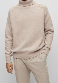 Ljust beige polotröja gjord av mjukt material, med ribbade mudd och nederkant, en avslappnad passform och texturmönster på axlarna.