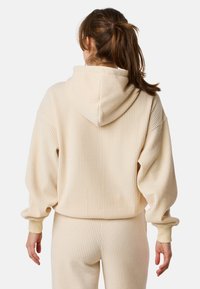 Felpa a coste color crema con cappuccio regolabile, vestibilità rilassata e maniche lunghe. Presenta una consistenza morbida e polsini elasticizzati.