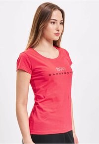 Red cotton t-shirt with a scoop neck, short sleeves, featuring printed text in black: “危ない” and “DANGEROUS” centrally placed.