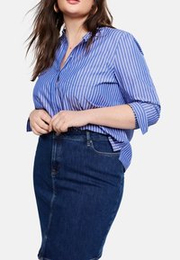 Camisa de botones a rayas azul y blanca combinada con una falda lápiz de mezclilla oscura. La camisa tiene mangas dobladas; la falda presenta un detalle de bolsillo frontal.