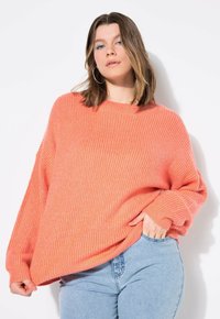 Maglione rosa corallo extralargo con texture a costine, scollatura a girocollo e spalle cadenti, abbinato a jeans azzurri chiari.