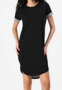 Czarna sukienka t-shirty z krótkimi rękawami. Szare akcenty na rękawach, zaokrąglony dekolt i lekko zakrzywiony dół z bocznymi rozcięciami. Miękka tkanina, casualowy fason.