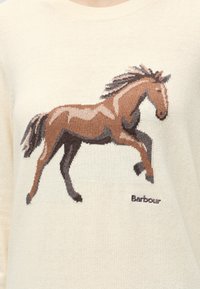 Motif tricoté d'un cheval marron au galop sur un pull crème avec le nom de la marque Barbour brodé sous le cheval.