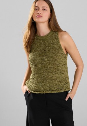Green knitted sleeveless top with a textured design, round neckline, and ribbed hem, paired with black wide-leg pants.