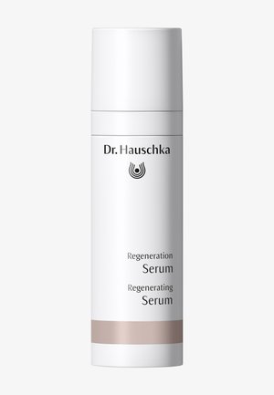 Bouteille cylindrique blanche étiquetée Dr. Hauschka Sérum Régénérant avec une bande beige près de la base sur un fond uni.