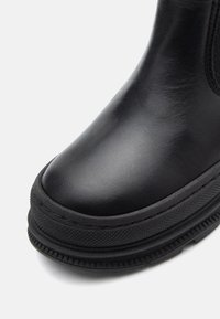 Botte waterproof noire avec un dessus en cuir lisse, semelle en caoutchouc texturé, bout rond et panneaux élastiques sur les côtés pour un enfilage facile.