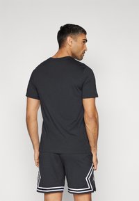 Camiseta negra de cuello redondo y mangas cortas, combinada con pantalones cortos negros perforados que tienen rayas blancas y un acento en el lateral.