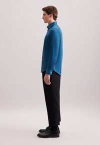 Teal shirt met lange mouwen, knoopmanchetten en een rechte snit, gecombineerd met zwarte broek en zwarte schoenen. Gladde stof textuur.