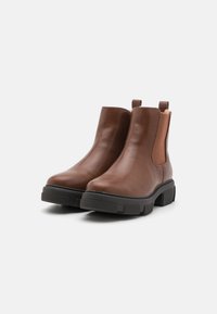 Bottines en cuir brun avec des panneaux latéraux élastiques et des systèmes de tirage, dotées d'une semelle en caoutchouc noir texturé et d'un design à bout arrondi.