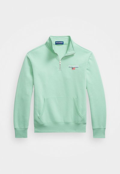Lys grøn quarter-zip pullover lavet af blødt stof, med en frontlomme og broderet logo på brystet i kontrasterende farver.