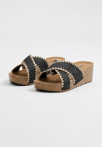 Sandalias de plataforma trenzadas en negro con tiras cruzadas, costuras decorativas en beige y suela texturizada similar al corcho. Plantilla interior suave.