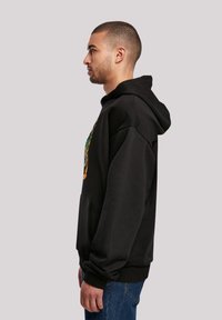 Svart hettegenser med en frontlomme, ribbestrikkede mansjetter, og et fargerikt grafisk design på brystet. Stoffet ser mykt og teksturert ut.